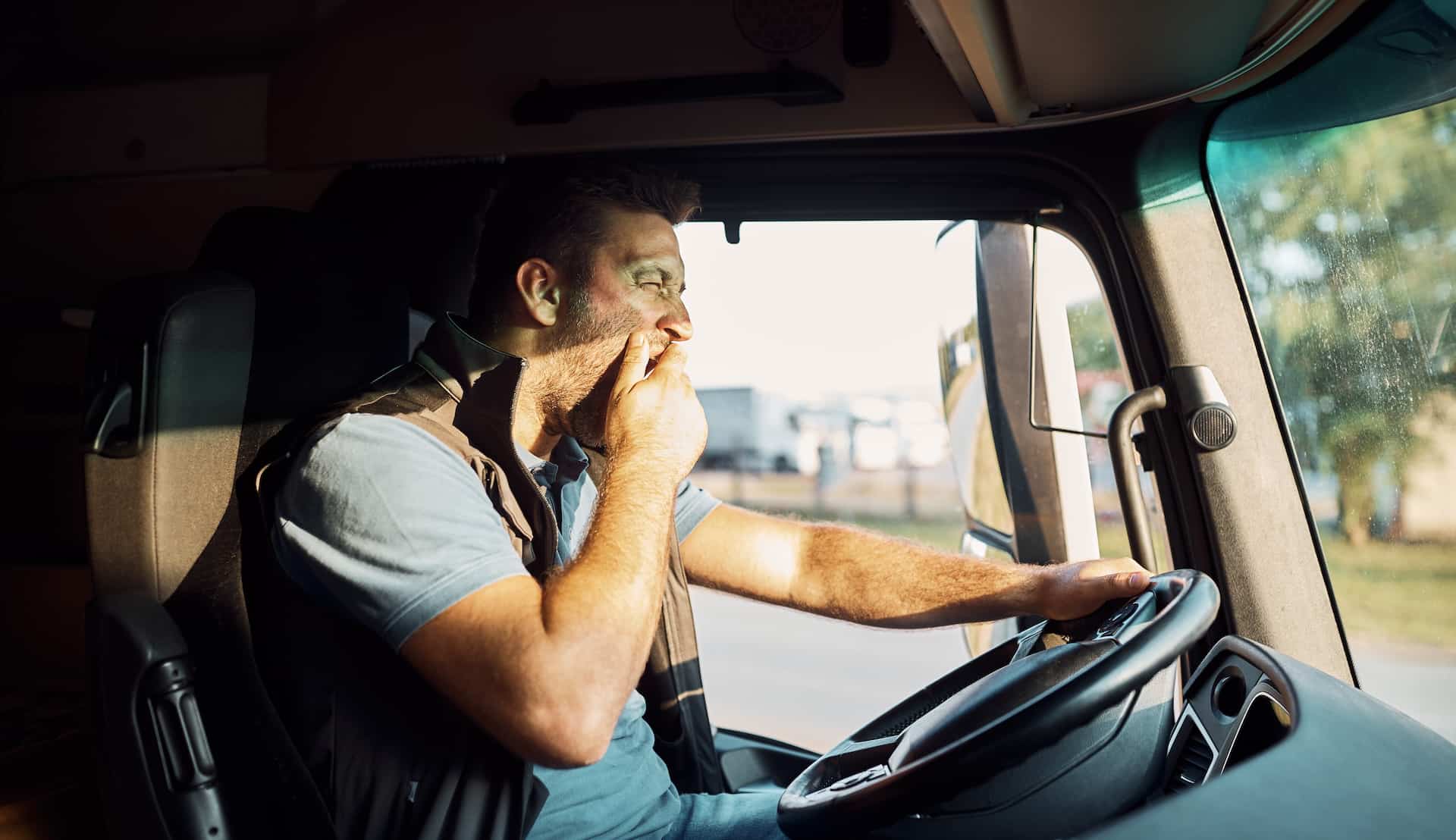 Tired truck driver yawning behind the steering wheel.